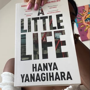 image of a girl holding a book titled a little life in front of her face